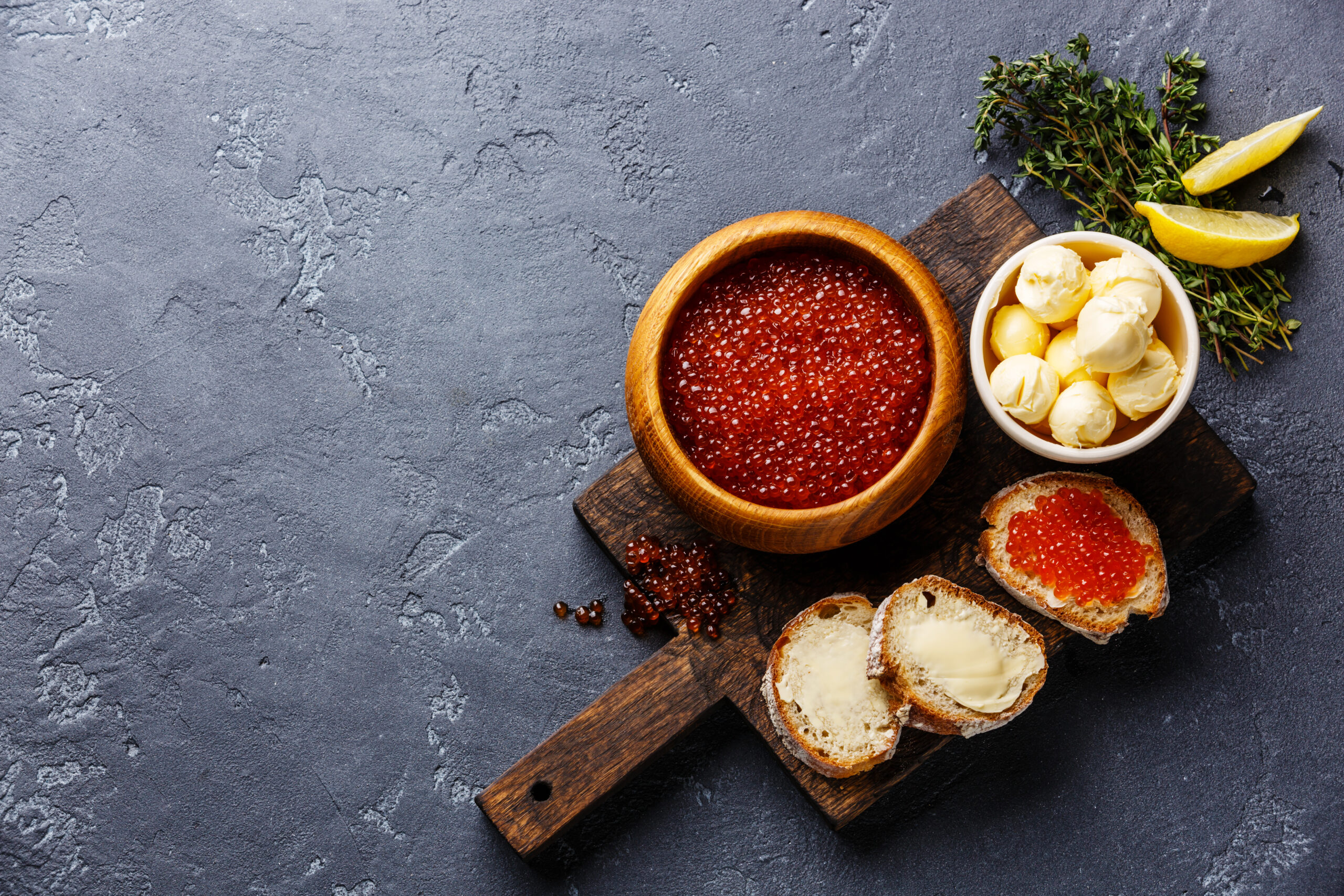 Salmon red caviar in wooden bowl and Sandwiches on dark stone background copy space